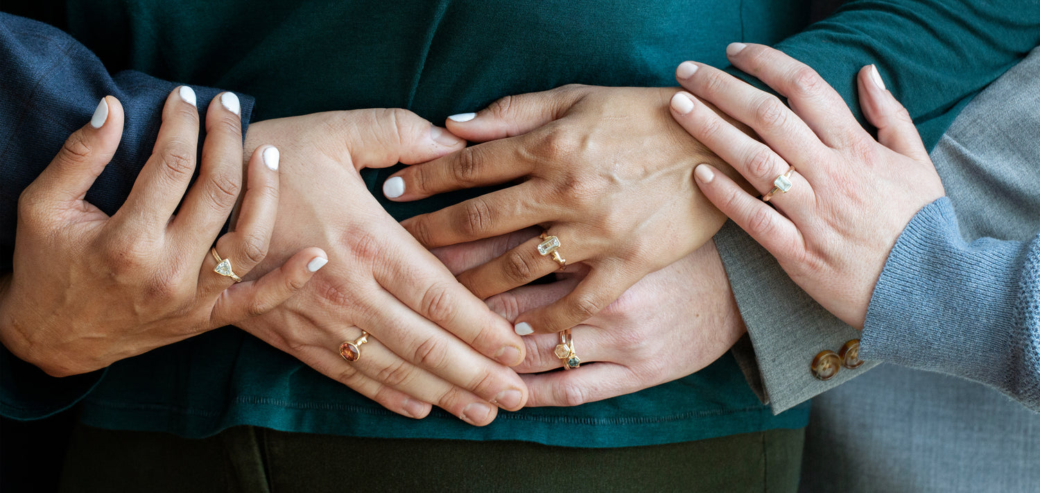 Peoples hands on top of each other, each wearing rings created by W.R. Metalarts, ethical jewelers.