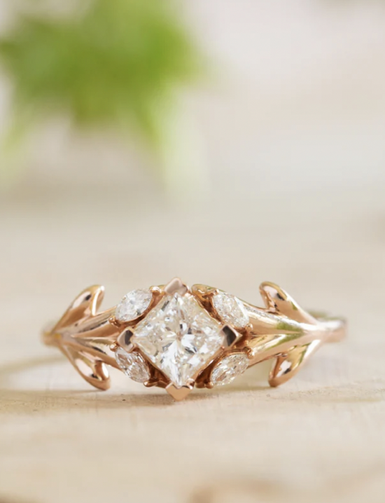 A Rose gold ring with olive branches which encircle marquise diamond leaves and a princess cut diamond, and Moroccan lattice-inspired setting to create an engagement ring that is both rustic and whimsical. Handcrafted by W.R. Metalarts, a US jeweler.