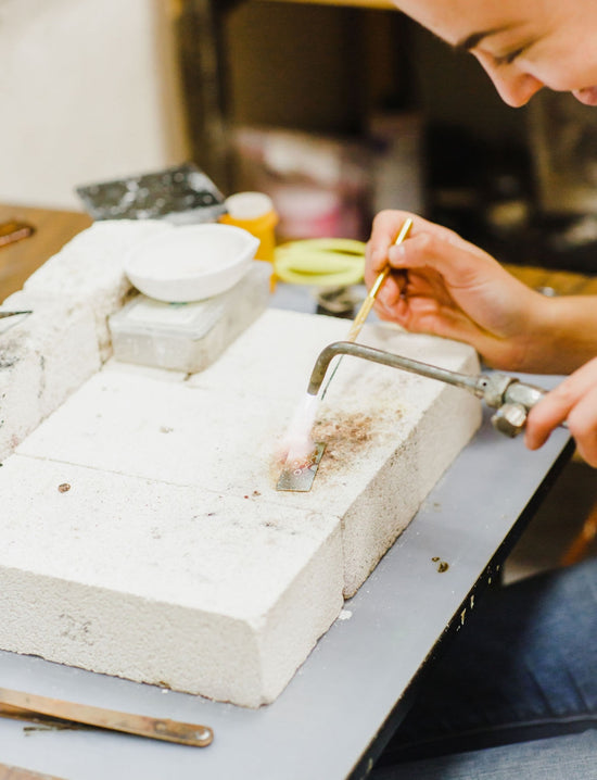 W.R. Metalarts Metalsmith soldering a piece of metal on a work top in her studio.