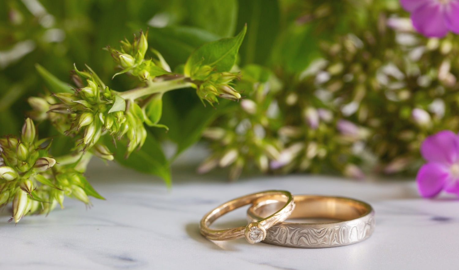 Image of Personal Gold Personal Stone White gold raindrop Mokume rings with flowers in the background. Created and made by W.R. Metalarts ethical jewelers 