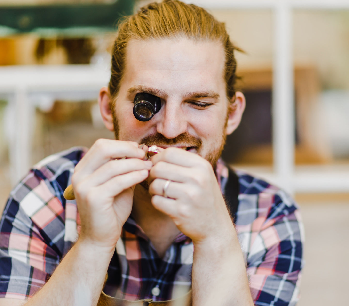 W.R. Metalarts founder Will Nevins-Alderfer smiling whilst holding and looking at a diamond ring through a small lense in his right eye.