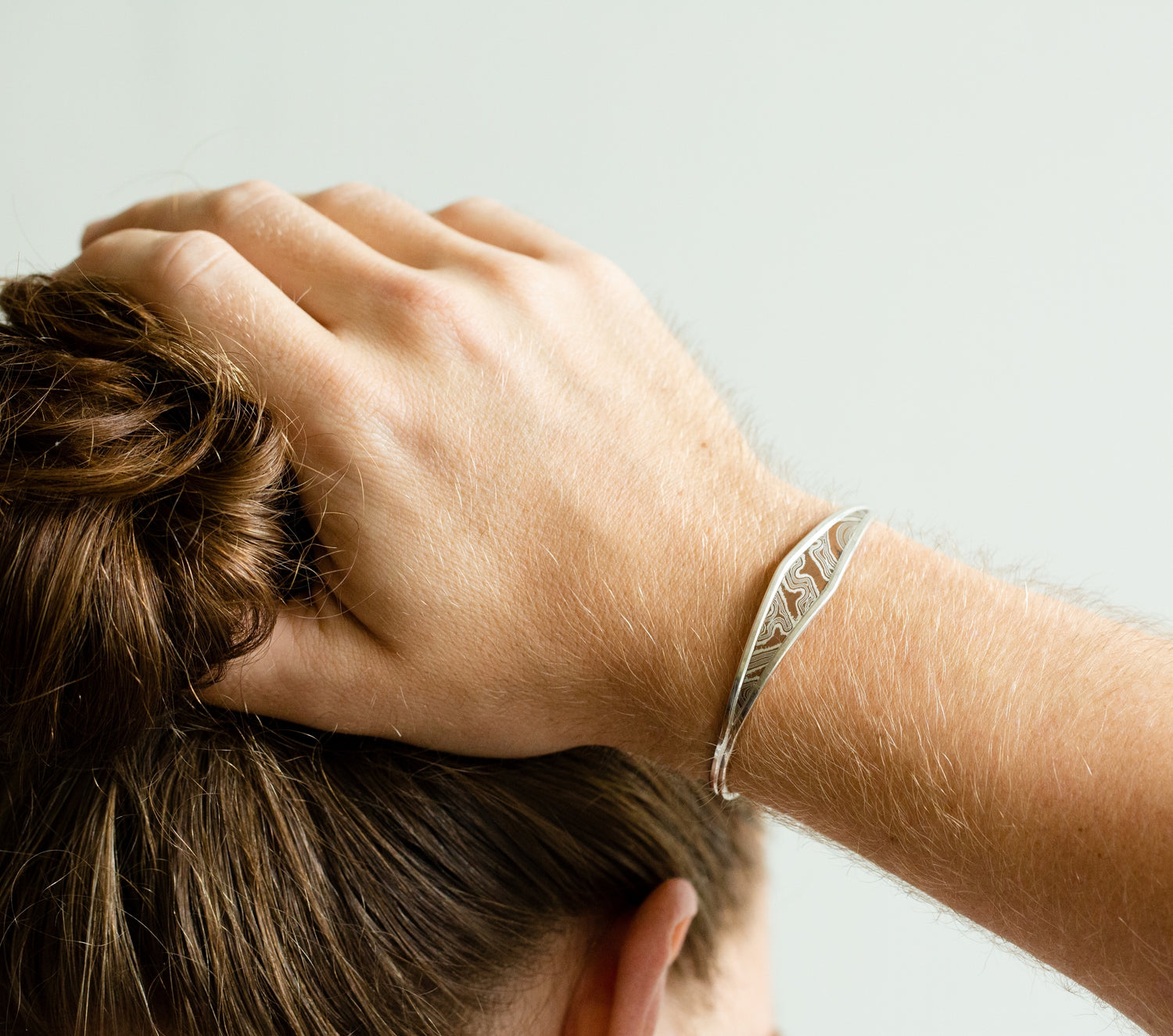Male with hand on his hair, wearing a mokume game bracelet created by W.R. Metalarts. All inclusive jewelers and metalsmiths